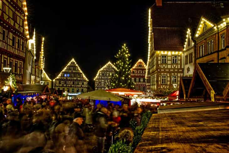 Božićni market na trgu koji je okružen osvetljenim kućama