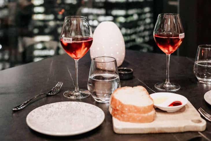 Dve čaše vina i hleb pored tanjira na stolu