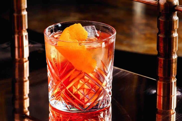 Kristalna čaša u kojoj je negroni piće sa ledom i korom pomorandže